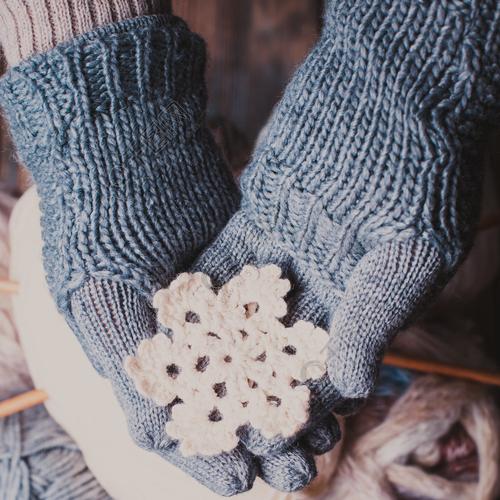 在拿着白色的灰色手套的手编织了雪花作为冬天标志戴着针织手套的手